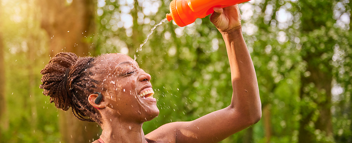 Femme se rafraîchissant en versant de l’eau sur sa tête tout en portant des écouteurs de sport Philips en extérieur